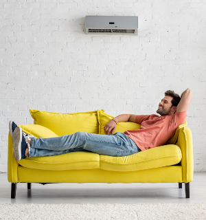 client fericit sta pe canapea sub aparatul de aer condiționat recent instalat